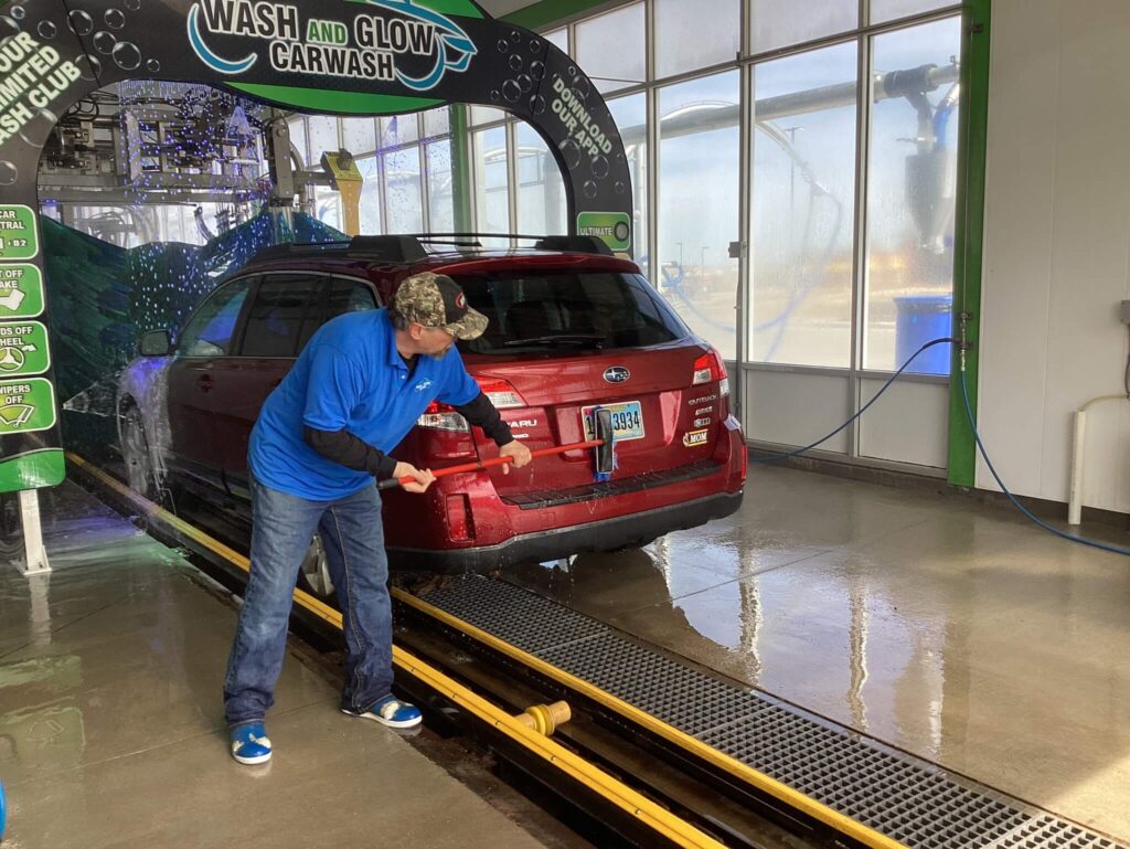 An attendant at Wash and Glow Car Wash wiping down the back of a car